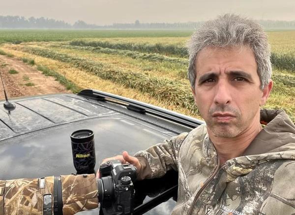 Photographer Gilad Kfir with camera and dressed in camo, looking into camera.