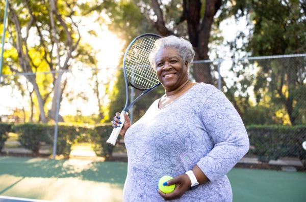 An older, overweight Black women holding a tennis racket