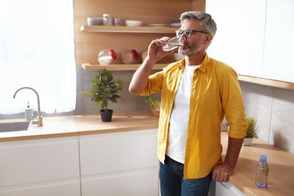 A man standing in a kitchen drinking a glass of water.