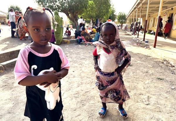 Children stand on a dirt track.